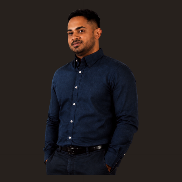 Faris Osmanbhoy standing with his hands in his pockets against a warm charcoal background.